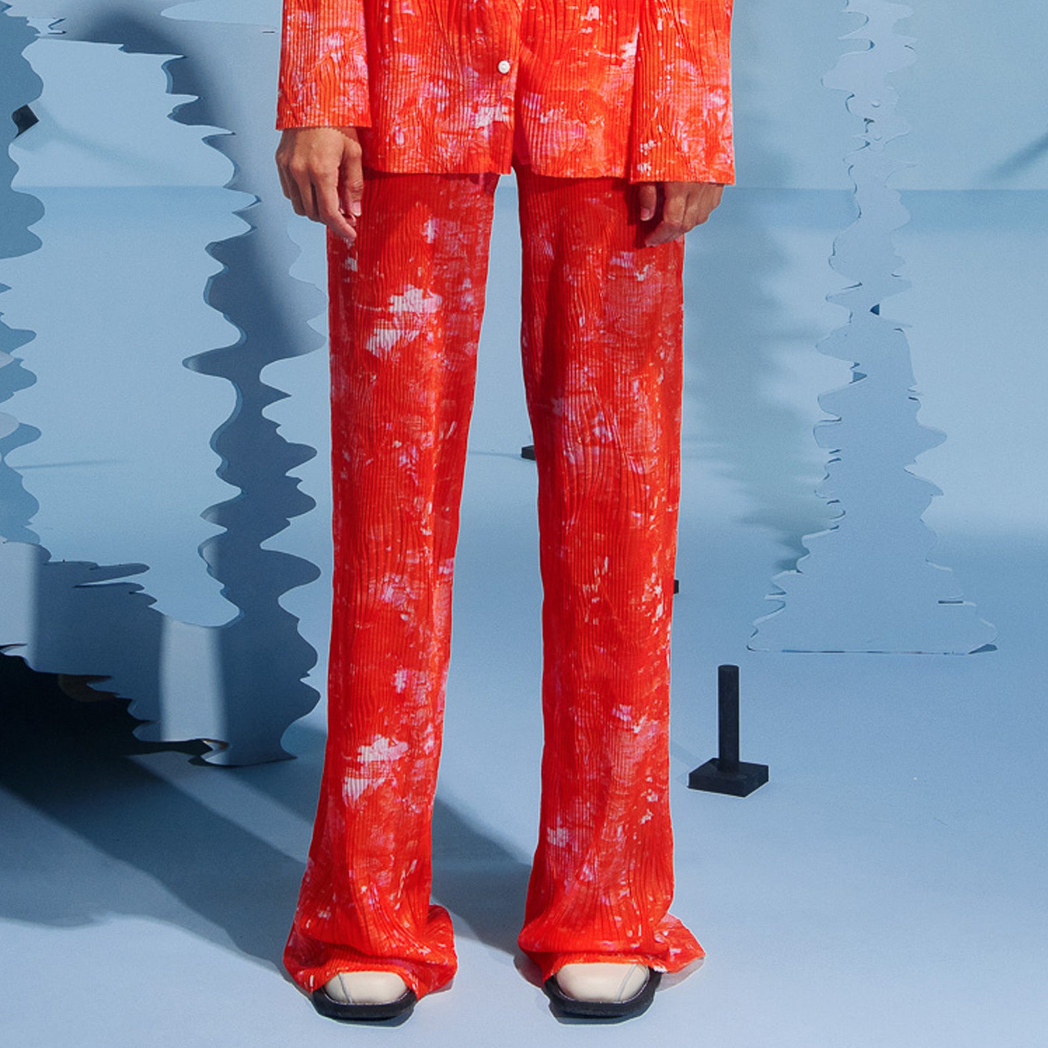 Pleated mesh pant in a orangey red pleated print, full length.
