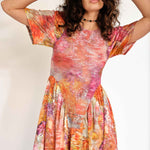 A model wears the Pollinate Dress in Chrysanthemum - multicolored floral dress with short bell sleeves and an asymmetrical ruffled hem - detail view.