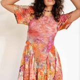 A model wears the Pollinate Dress in Chrysanthemum - multicolored floral dress with short bell sleeves and an asymmetrical ruffled hem - detail view.