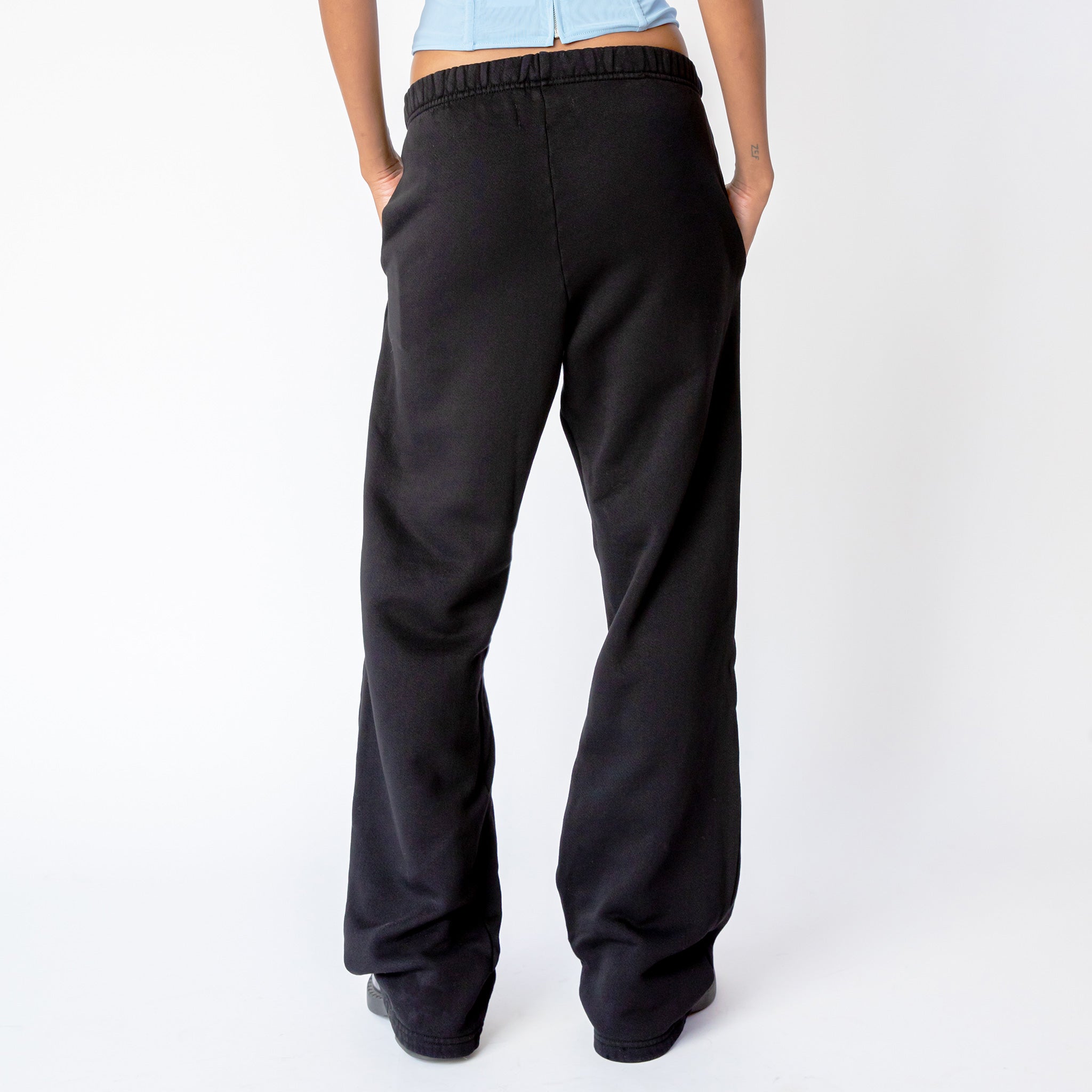 A model wears the Les Tien Puddle Pant in Jet Black, a long, straight-legged sweatpant with extra length that puddles at the feet - back view.