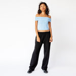 A model wears the Les Tien Puddle Pant in Jet Black, a long, straight-legged sweatpant with extra length that puddles at the feet - paired here with a light blue off-shoulder corset, full outfit view.