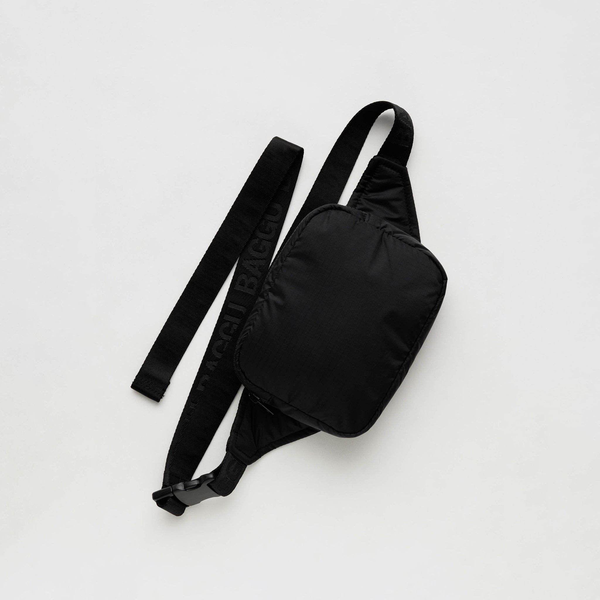 A rectangular black nylon fanny bag with the shell of the bag in a puffy fabric and repeating BAGGU logo debossed on the black nylon straps.