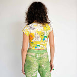 Yellow baby tee with illustrative graphic and white PUPPIES letters printed across the chest over a large heart symbol - back view.