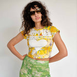 Yellow baby tee with illustrative graphic and white PUPPIES letters printed across the chest over a large heart symbol - front view.