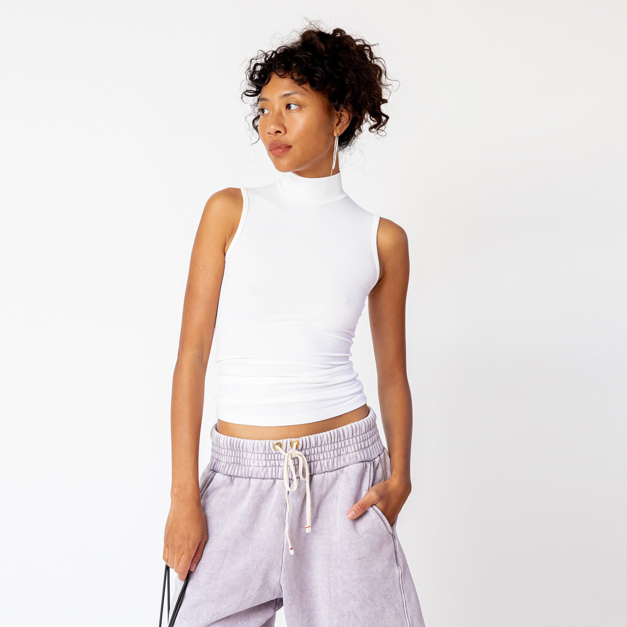 A model wears a sleeveless white mockneck tank top in white - front view.