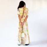 Back view of a model wearing the Ritual Dress - Light Chrysanthemum, a full length short-sleeved printed dress with a long vertical slit down the back.
