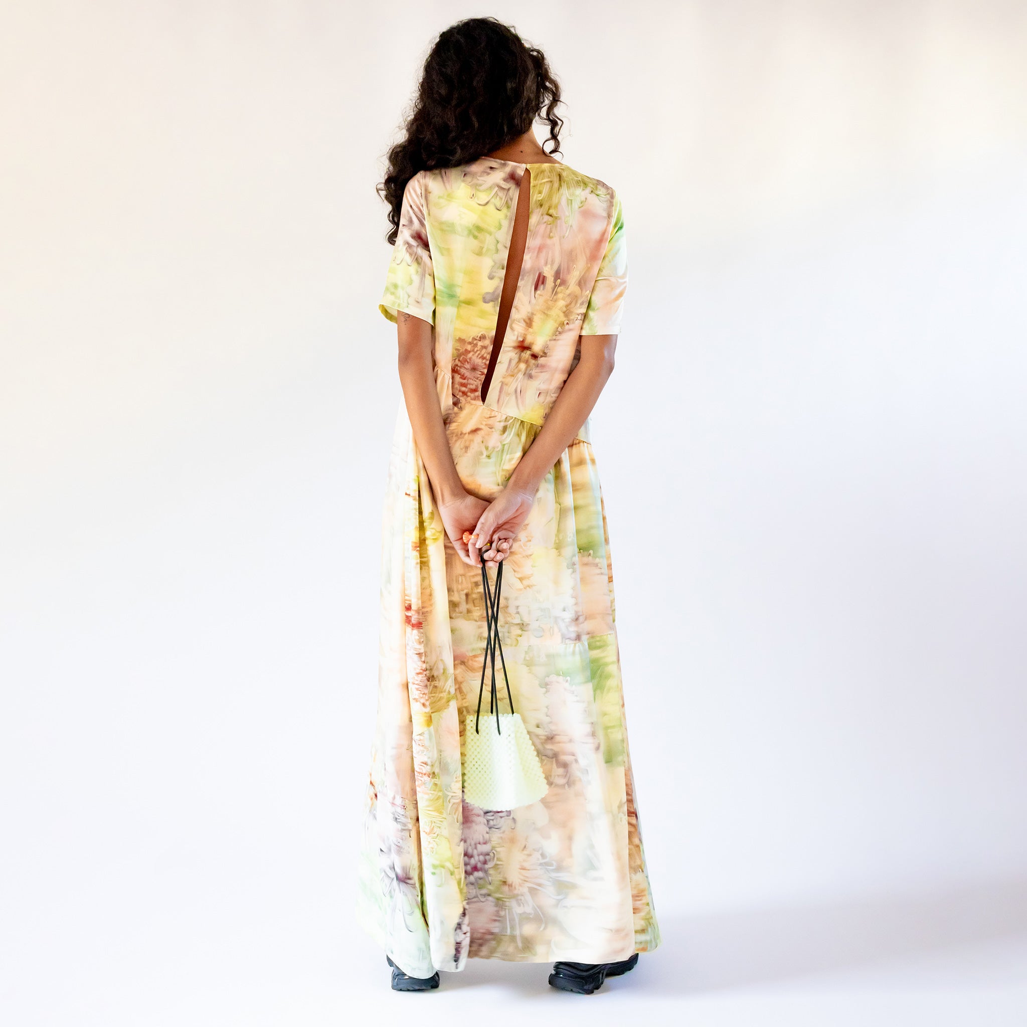 Back view of a model wearing the Ritual Dress - Light Chrysanthemum, a full length short-sleeved printed dress with a long vertical slit down the back.