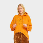 A model wears the Round Hem Cool Hoodie in Orange, which features a rounded hem and a roughly drawn embroidered graphic on the front with the letters 'cool'.