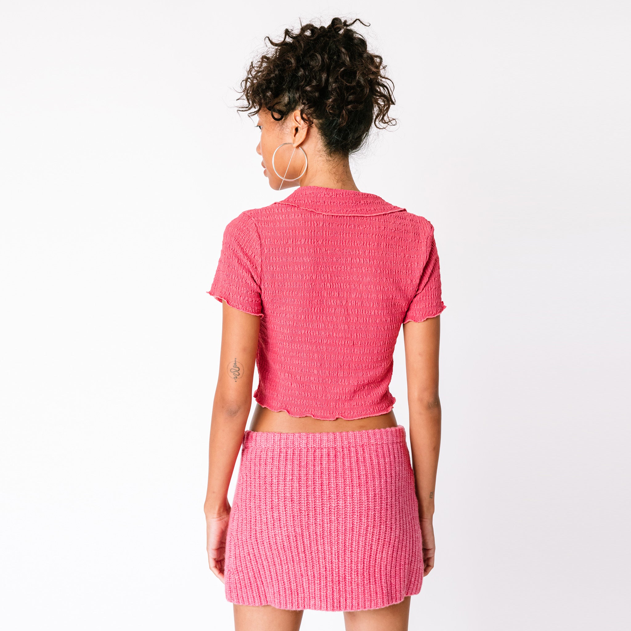 A model wears Misc Etc's pink ruched polo top in dark rose, paired with a matching pink mini skirt, back view.