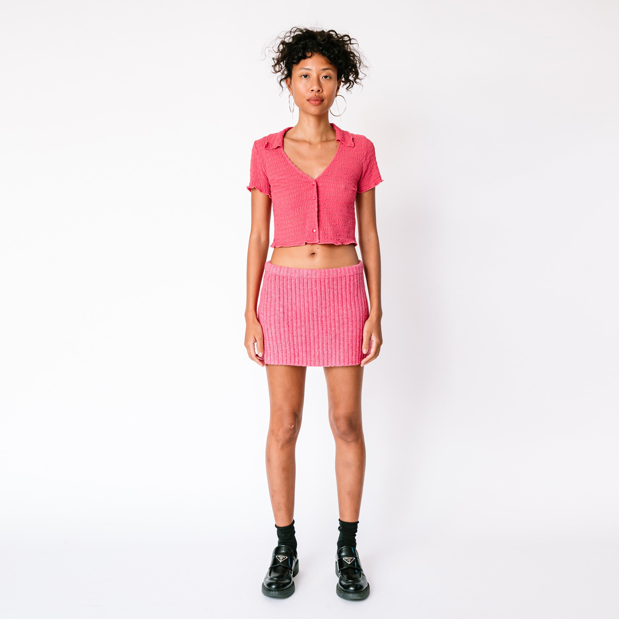 A model wears Misc Etc's pink ruched polo top in dark rose, paired with a matching pink mini skirt and black loafers, full outfit view.