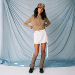 A model wears the lightweight brown cardigan by Sandy Liang paired with a white mink skirt and black loafers, full outfit view.