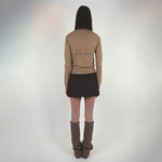Back full body photo of model wearing the Seek Sweater paired with brown knit leg warmers and a dark brown mini skirt. 