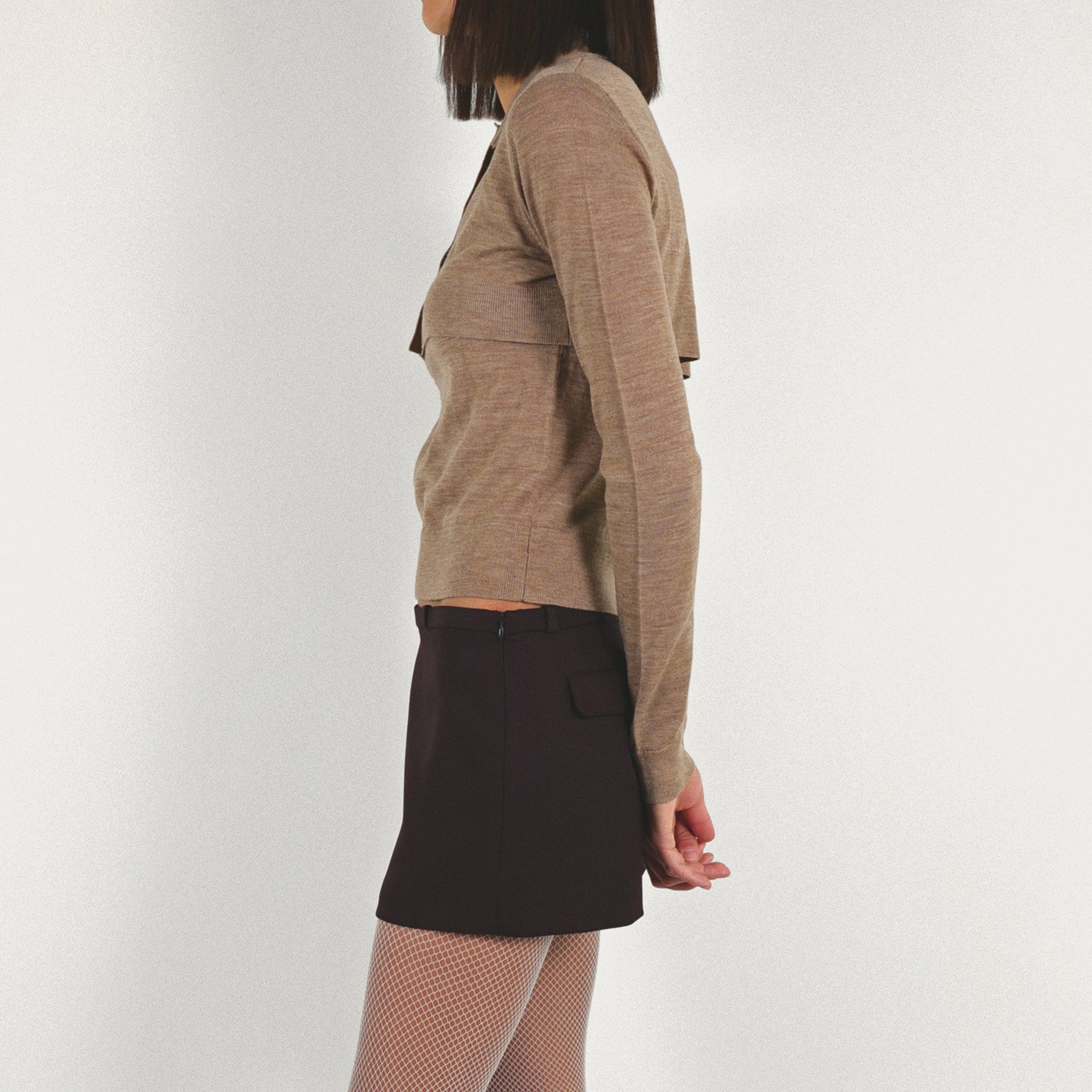 Side Half body photo of model wearing the Seek Sweater paired with a dark brown mini skirt. 