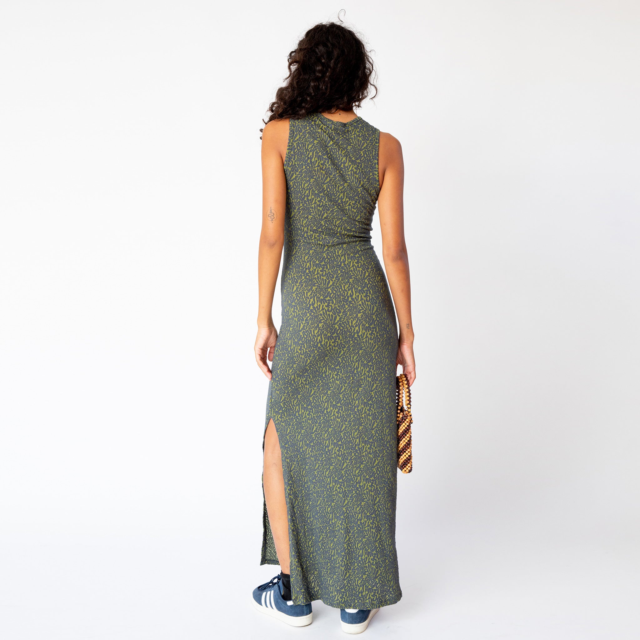 A model wears the form-fitting Shrunk Dress by Eckhaus Latta, a sleeveless full length casual dress in a green printed pattern, back view.