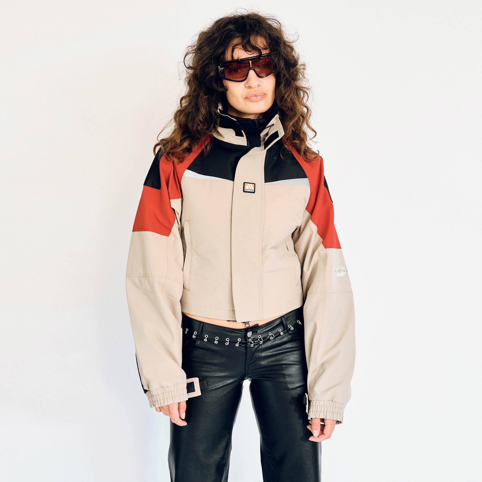 A model wears the Martine Rose Shrunken Sports Jacket with beige body and red and black color blocking on the shoulders.
