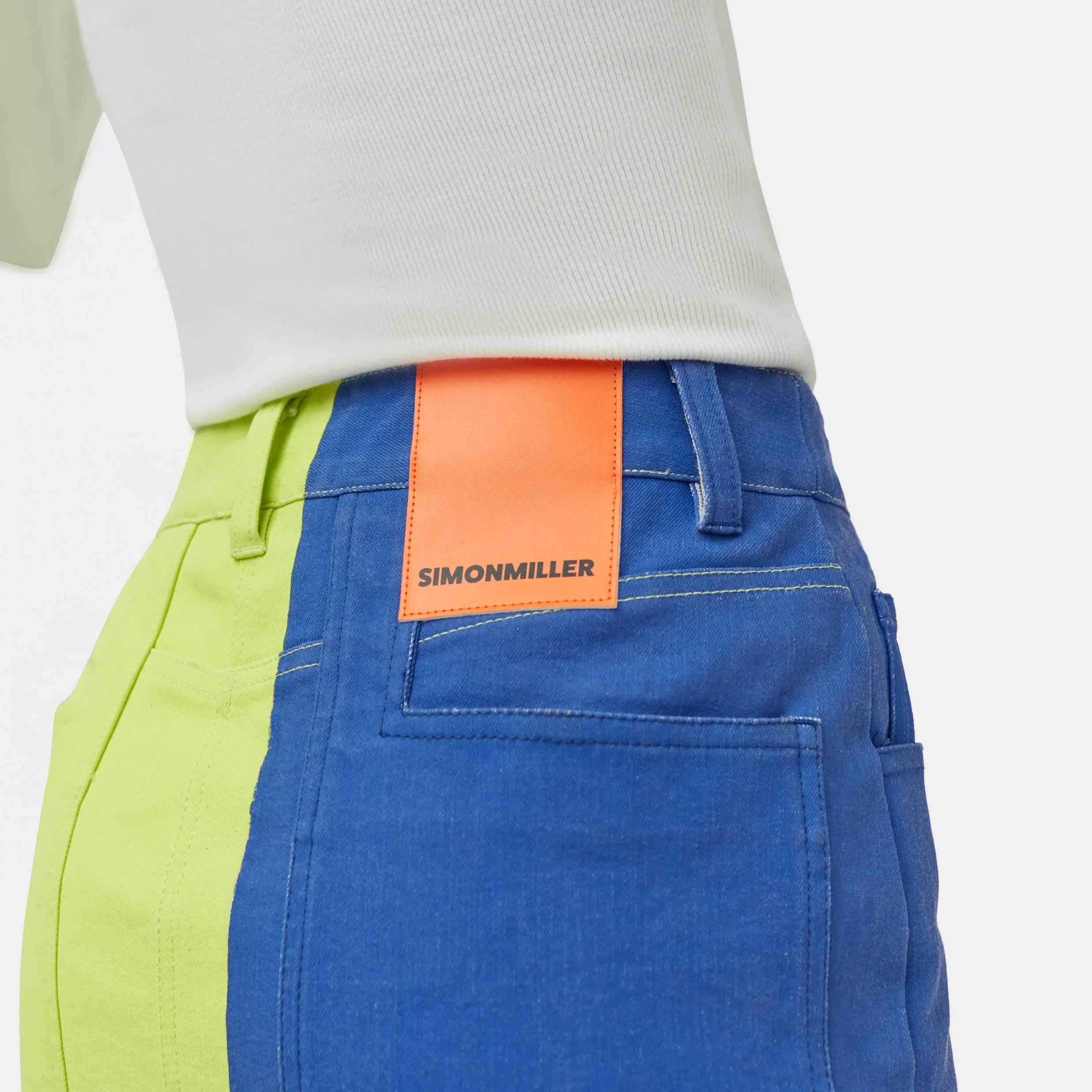 Close half body photo of model wearing the Simi Skirt - a full length denim skirt painted in color blocks of chartreuse, blue, and white - view of the back pocket and Simon Miller patch.