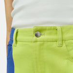 Close half body photo of model wearing the Simi Skirt - a full length denim skirt painted in color blocks of chartreuse, blue, and white - detailed view of the front button.
