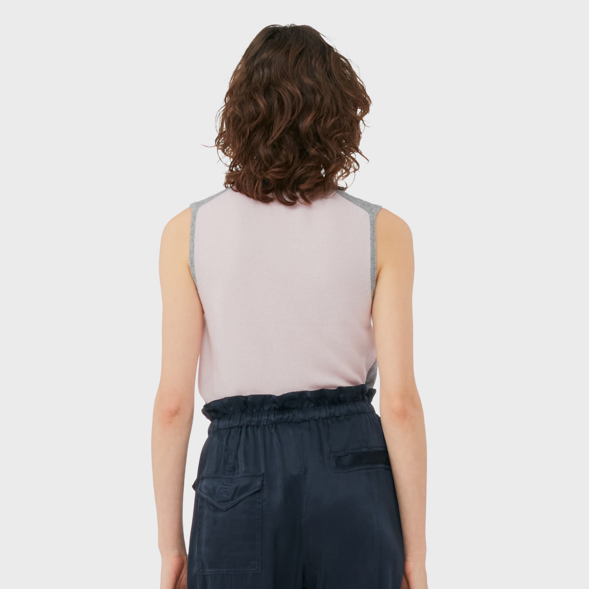 A model wears the frost gray sleeveless polo top with contrasting navy blue collar and gold button hardware, back view with semi-sheer white back.