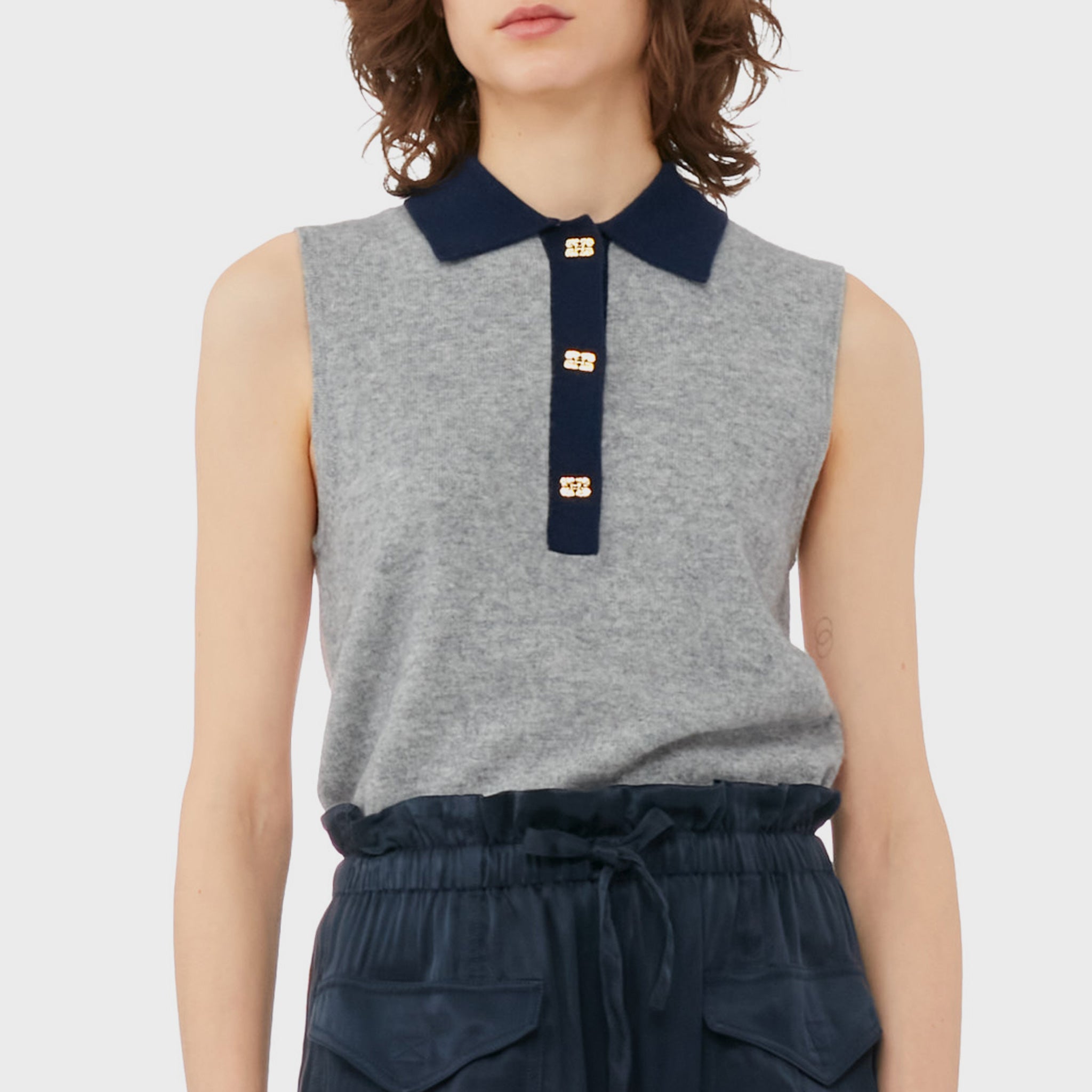 A model wears the frost gray sleeveless polo top with contrasting navy blue collar and gold button hardware.