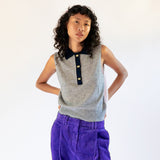 A model wears the frost gray sleeveless polo top with contrasting navy blue collar and gold button hardware.