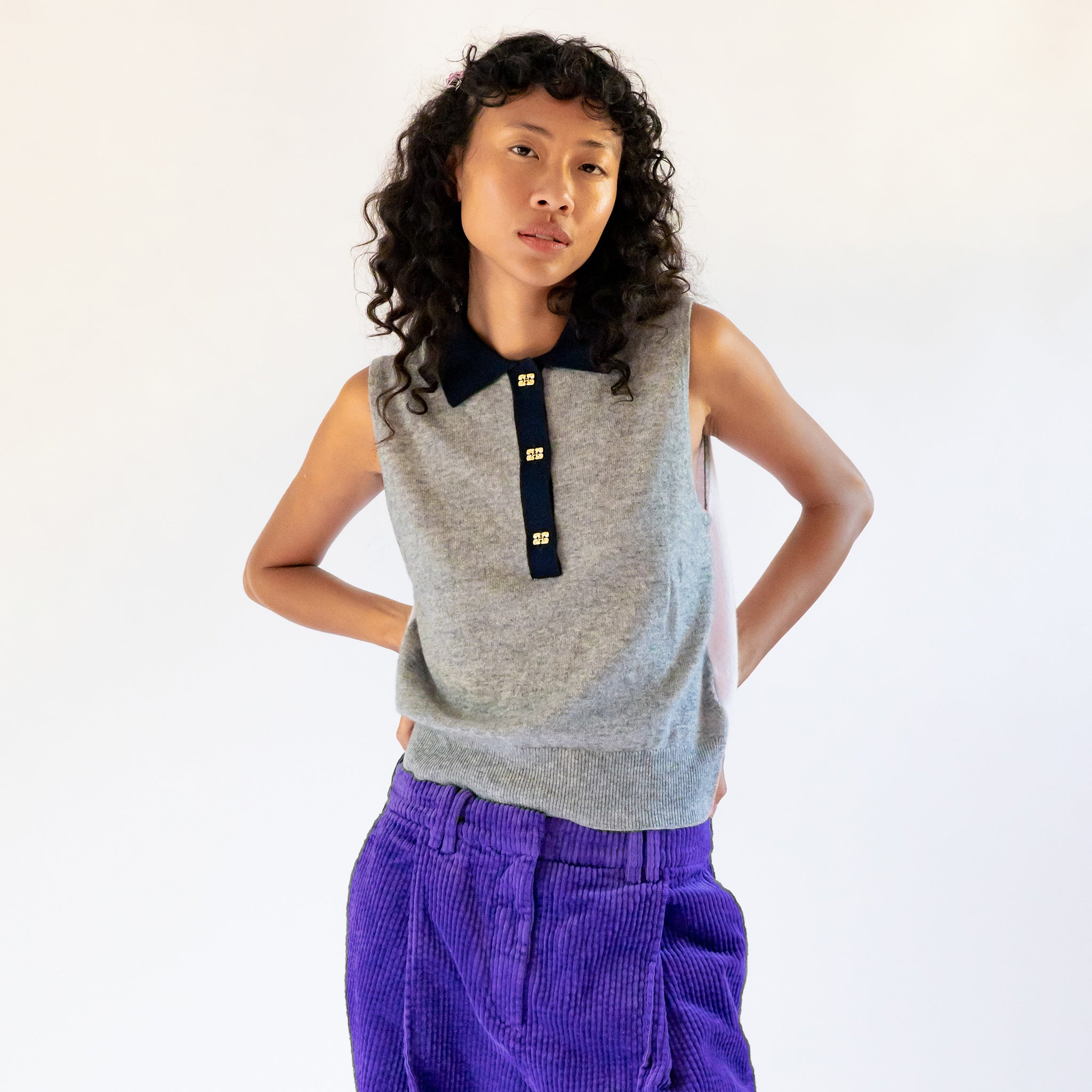 A model wears the frost gray sleeveless polo top with contrasting navy blue collar and gold button hardware.