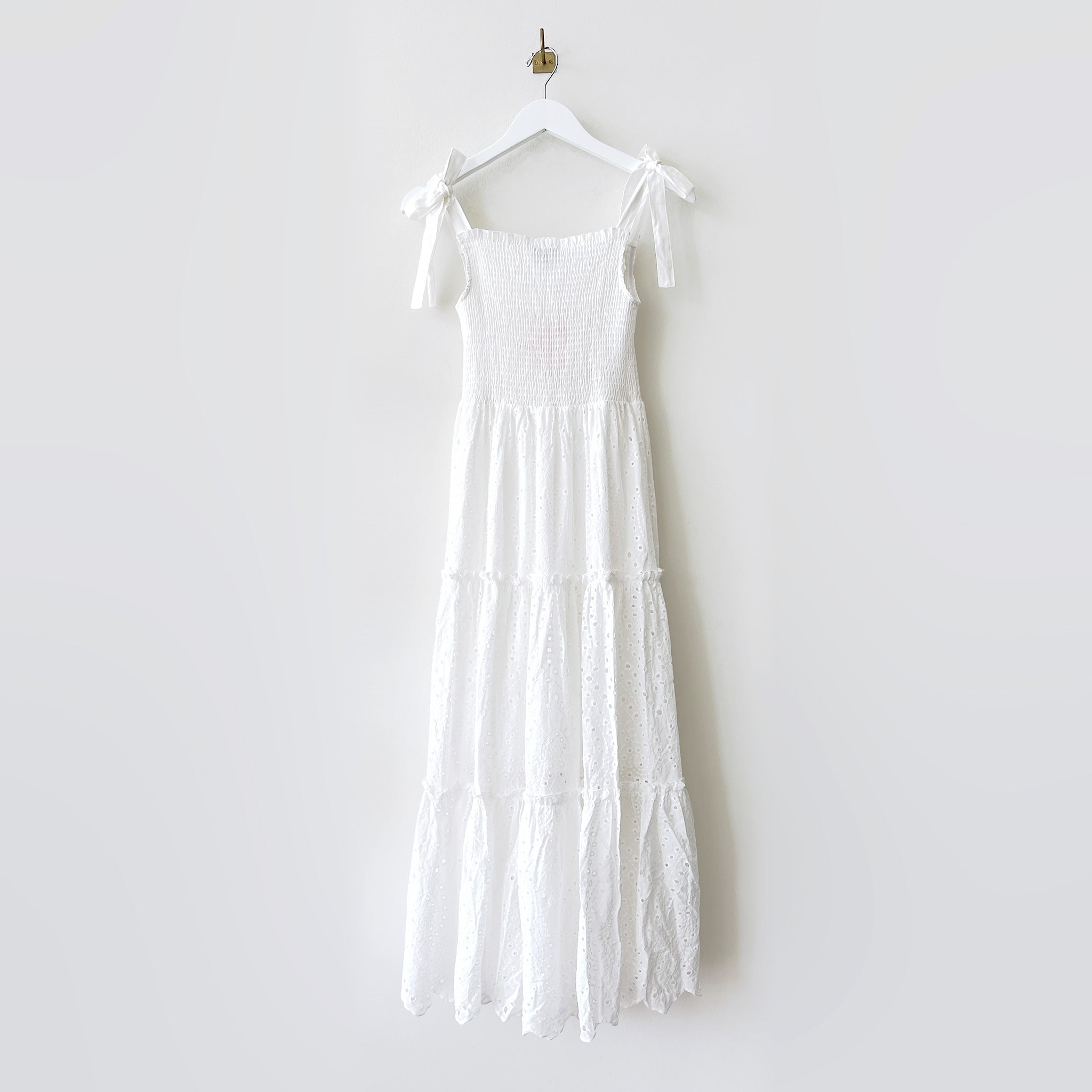 Long white dress with ruched bodice, ribbon tied shoulder straps and tiered eyelet skirt - back view.