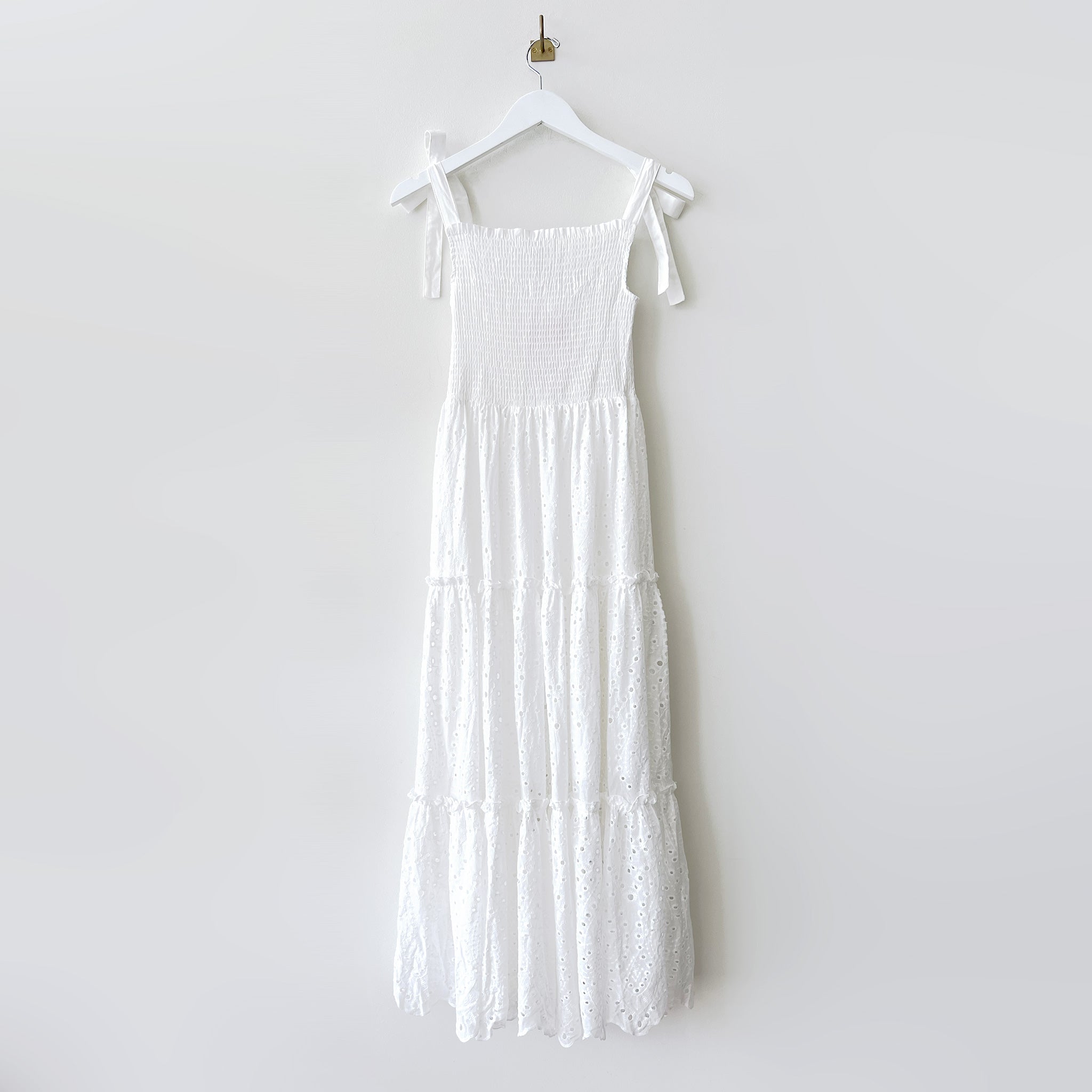 Long white dress with ruched bodice, ribbon tied shoulder straps and tiered eyelet skirt - front view.