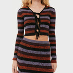 A model wears the black, red, and lavender striped cropped cardigan featuring black bow ties down the chest in place of buttons.