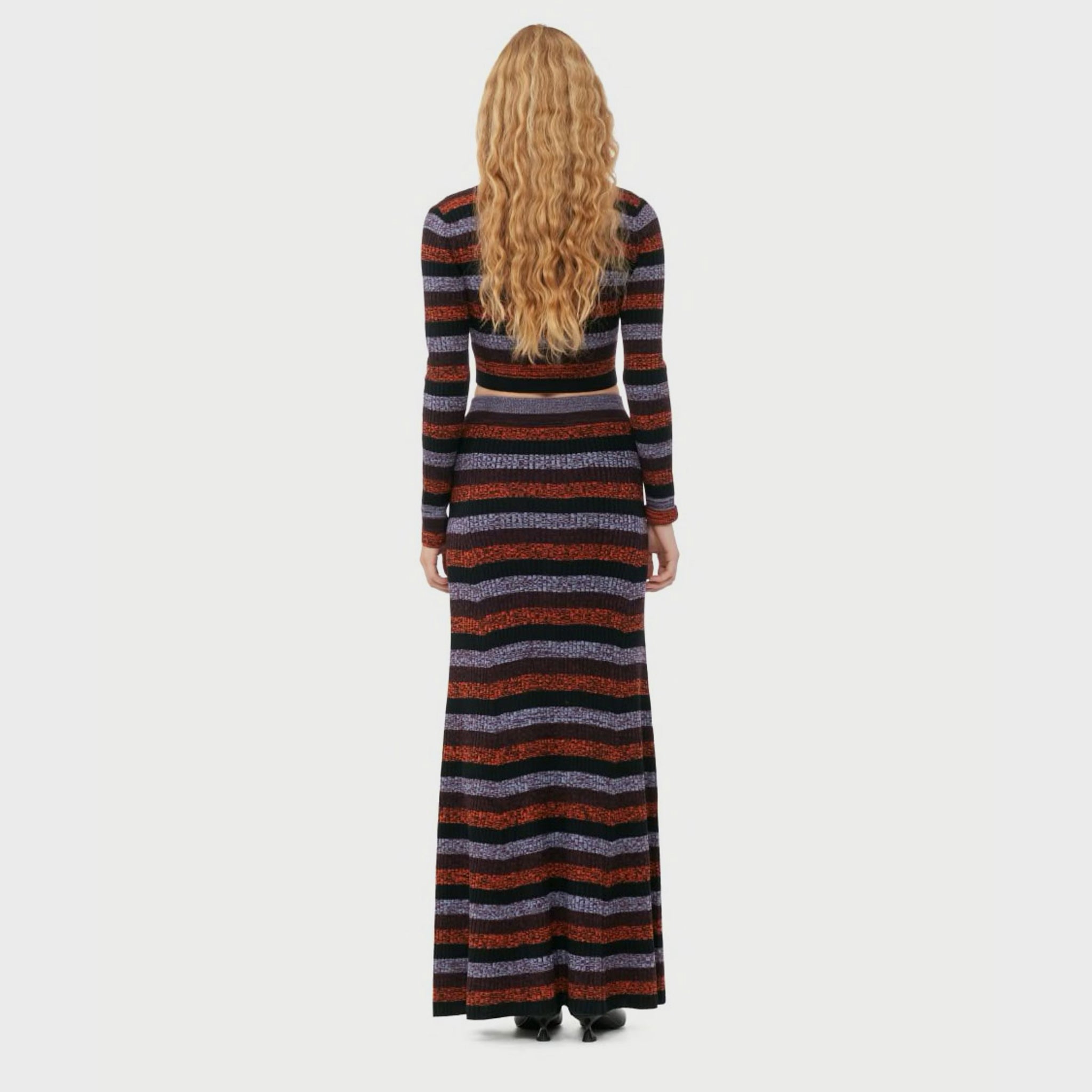 A model wears the black, red, and lavender striped maxi skirt, back view with matching cropped cardigan.