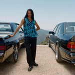 Photo of model wearing the Stacked Sweater Vest - Dark Navy standing in between two vintage cars.