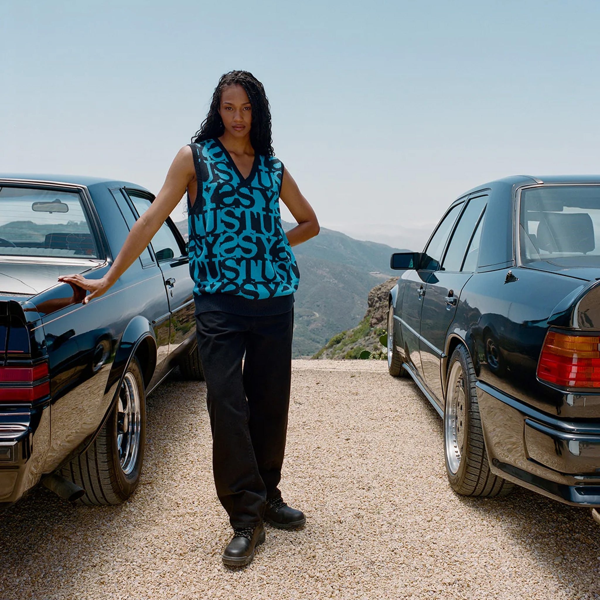 Photo of model wearing the Stacked Sweater Vest - Dark Navy standing in between two vintage cars.