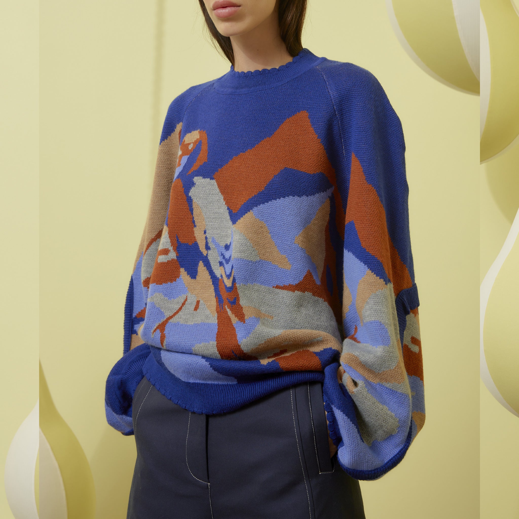 A model wears the blue oversized Stamp Sweater with abstract knit graphics in orange and grey.