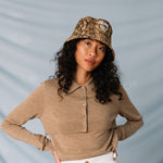 A model wears the Stock Lock Deep Bucket Hat by Stussy featuring an allover python brown print and white Stussy logo embroidery.