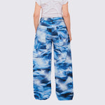 A model wears the cotton wide-legged Stomp Pant, featuring a blue and white aquatic inspired all over print, large front and side pockets, back view.