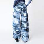A model wears the blue and white graphic dolphin printed, wide leg Stomp Pant by Collina Strada with matching mesh top and gloves - back view.