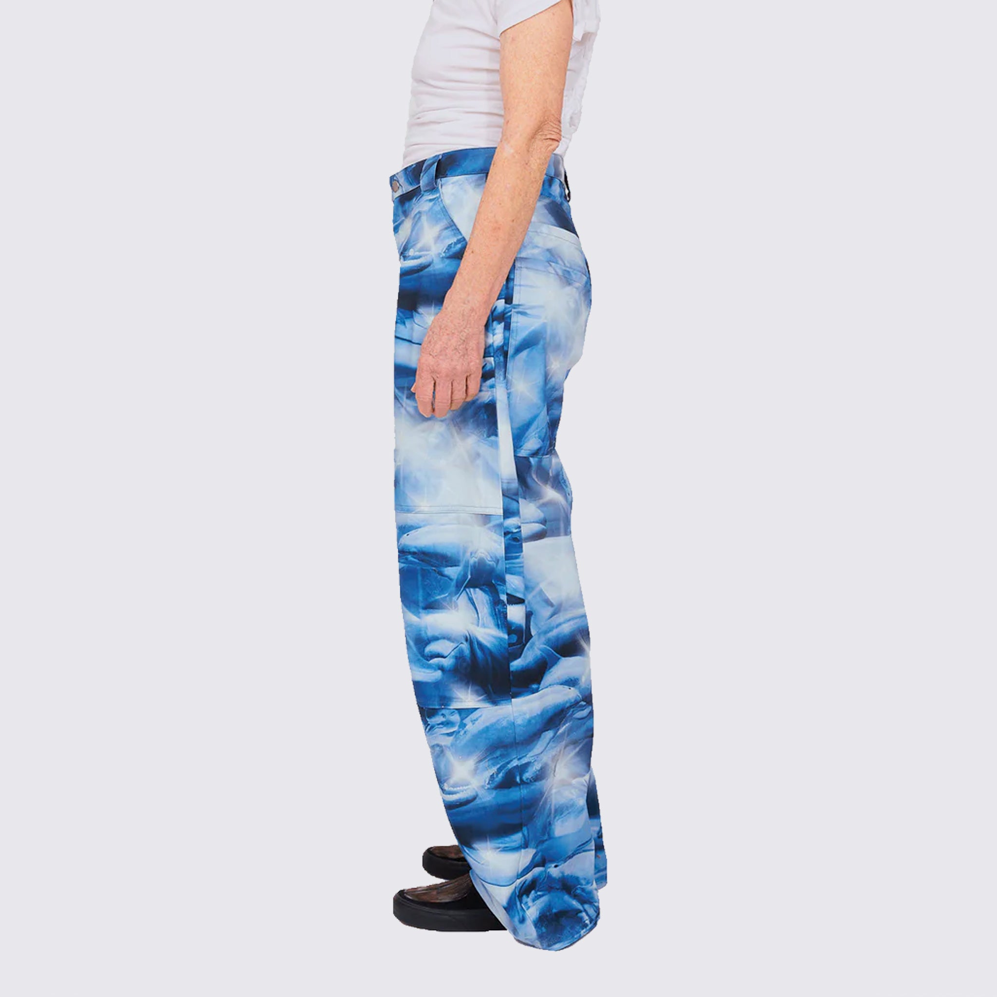 A model wears the cotton wide-legged Stomp Pant, featuring a blue and white aquatic inspired all over print, large front and side pockets, side view.