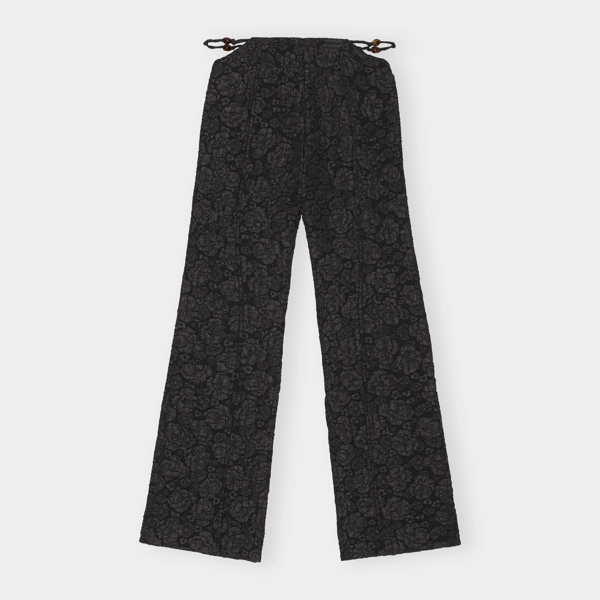 Black floral jacquard trousers with a slightly flared leg and featuring side waist cutout details exposing a thin twisted rope belt - back view.