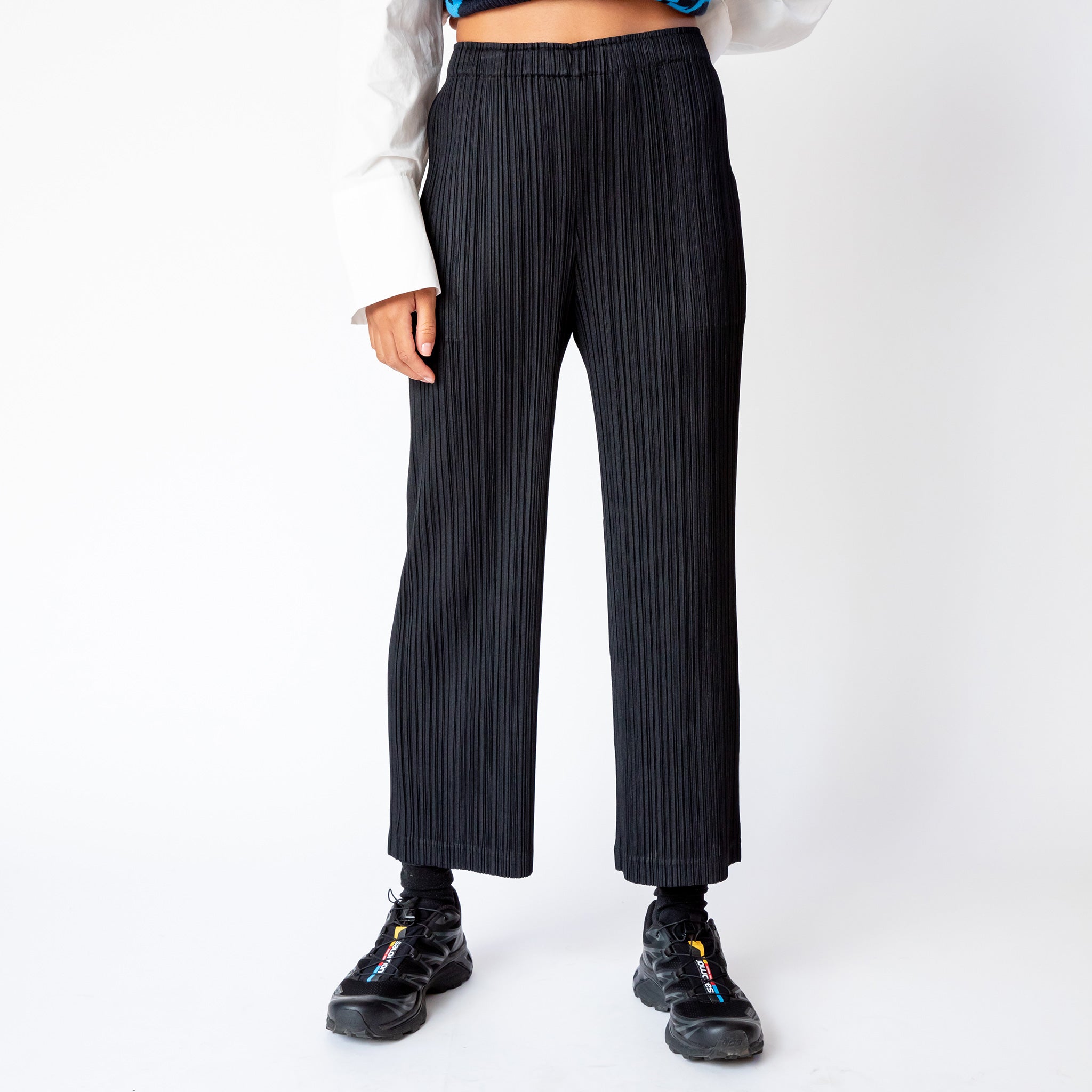 A model wears the black Thicker Bottoms 2 pleated trousers by Pleats Please, paired with black sneakers.