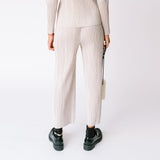 A model wears the light grey pleated Thicker Bottom 2 Pants by Pleats Please with matching hoodie and black loafers - back view.