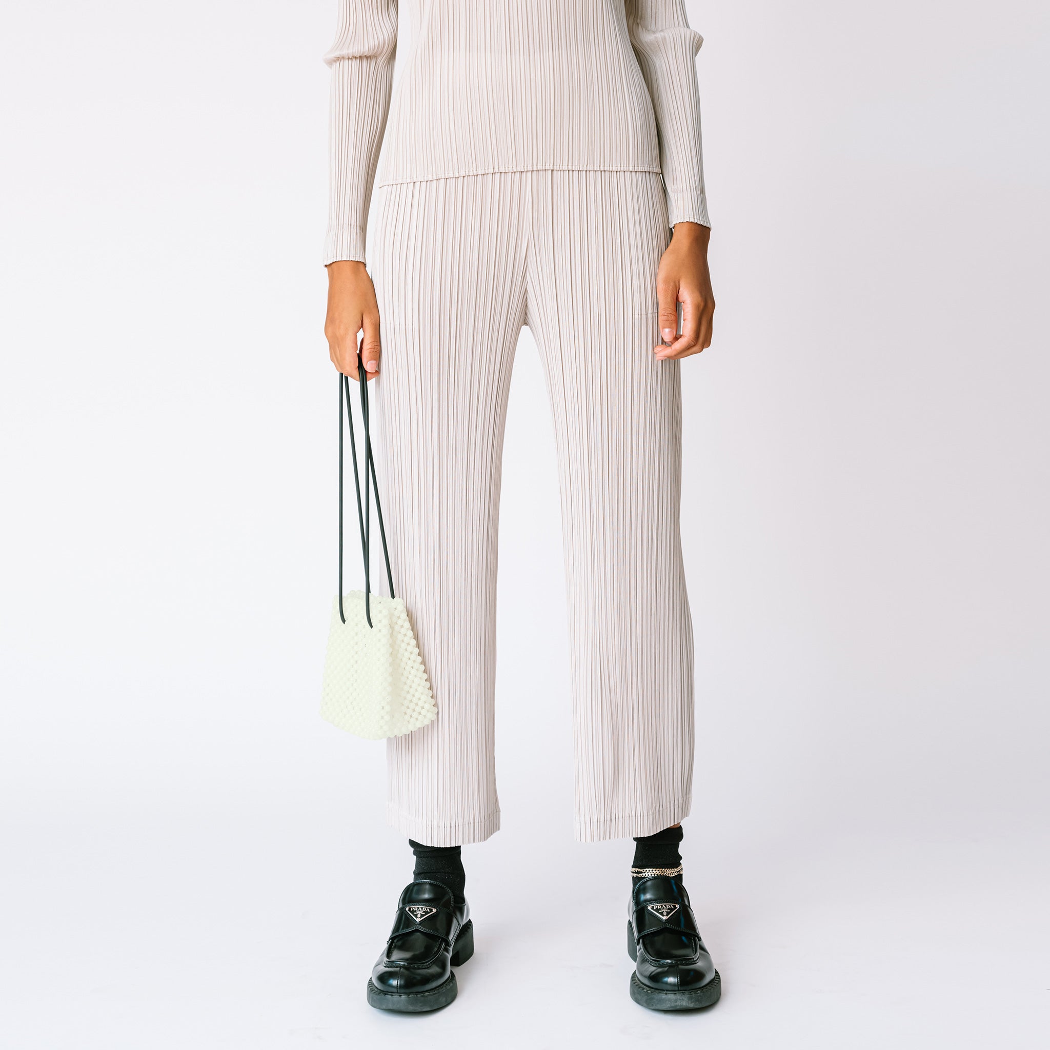 A model wears the light grey pleated Thicker Bottom 2 Pants by Pleats Please with matching top and black loafers.