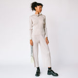A model wears the light grey pleated Thicker Bottom 2 Pants by Pleats Please with matching hoodie and black loafers.