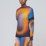 A lightweight long sleeve pleated top with a vibrant radial printed all-over graphic with orange, black and blue hues, angled view on model.