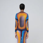 A lightweight long sleeve pleated top with a vibrant radial printed all-over graphic with orange, black and blue hues, back view on model.