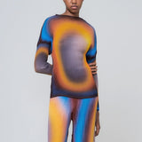 A lightweight long sleeve pleated top with a vibrant radial printed all-over graphic with orange, black and blue hues, on a model with one hand behind her back.