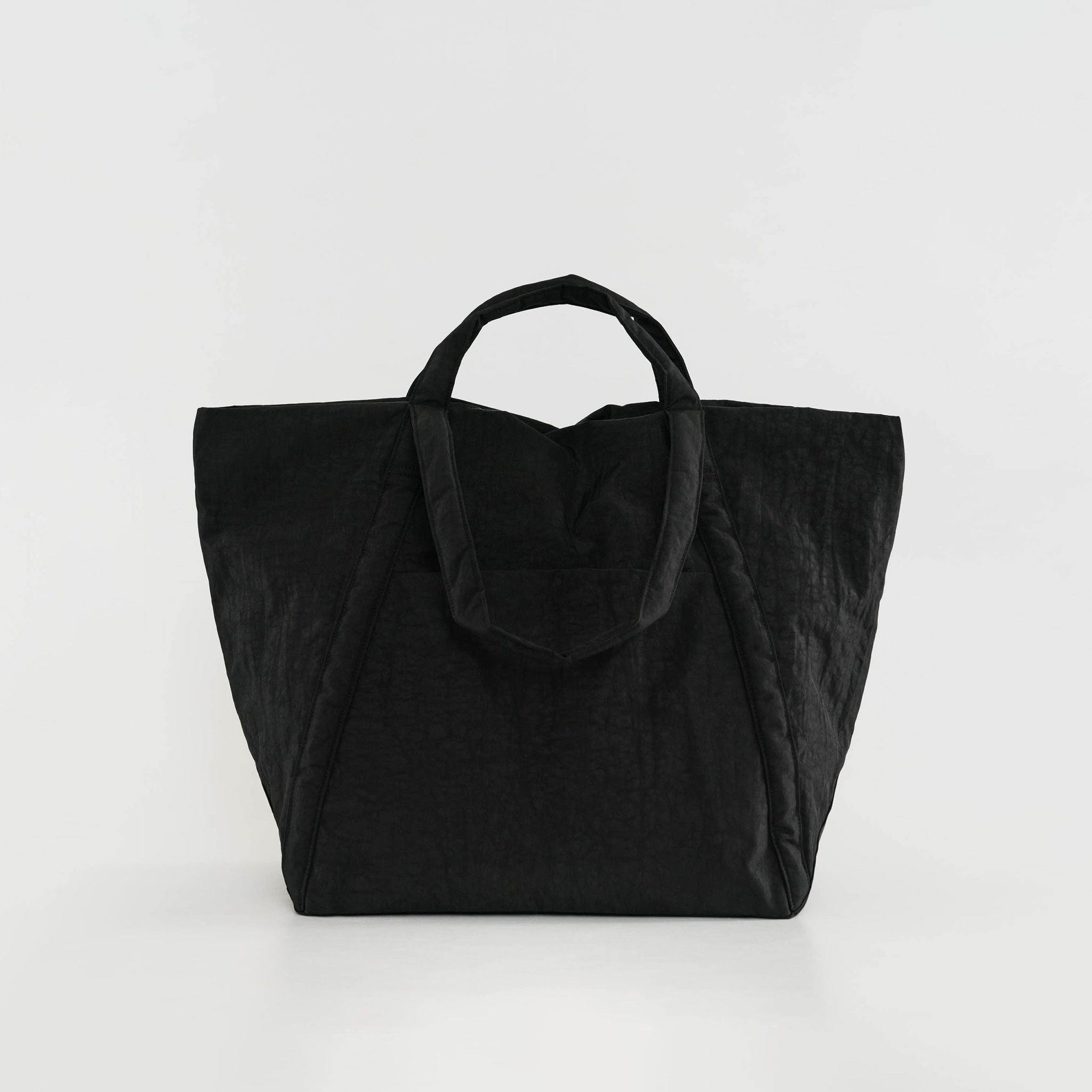 A large trapezoidal black nylon tote bag meant for traveling, fabricated in a puffy crinkly fabric, shown standing up.