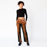 A model looks to the side while wearing Eckhaus Latta's wide leg jeans in ozone, featuring a vertical stripe of rust brown that gradients to black along the sides of the leg, paired with a cropped longsleeved black top and brown velvet pleated belt.