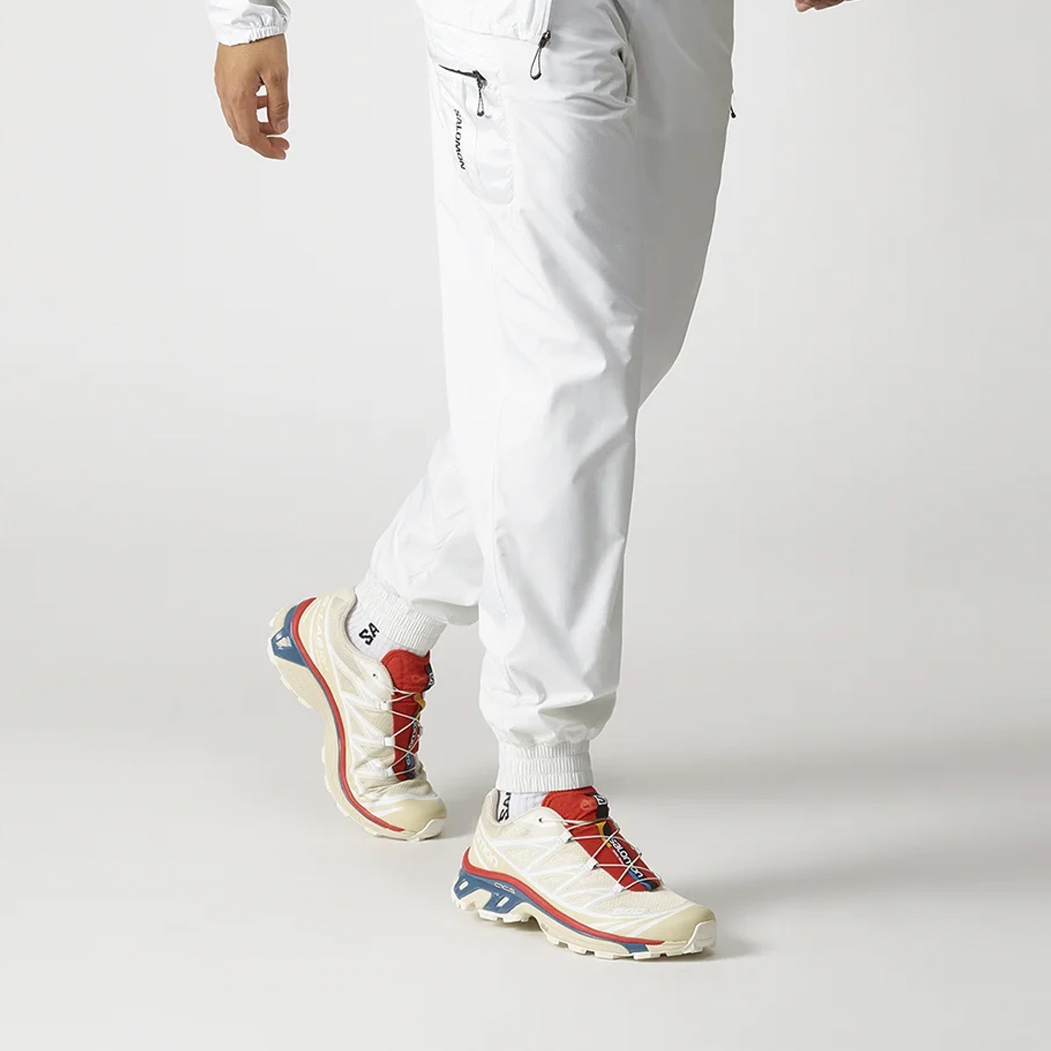 Off white XT-6 Salomon Sneakers with vibrant red and teal blue sole details, as worn by a male model.