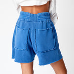 A model wears the Les Tien Yacht Short in electric blue, which feature a wide ruched elastic waistband, long white drawstrings, and an unfinished hem - back detailed view of the large back pockets with unfinished edges.