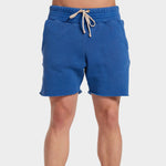 A male model wears the electric blue cotton Yacht Short by Les Tien, featuring a wide elastic waistband and long white waist ties and side pockets.