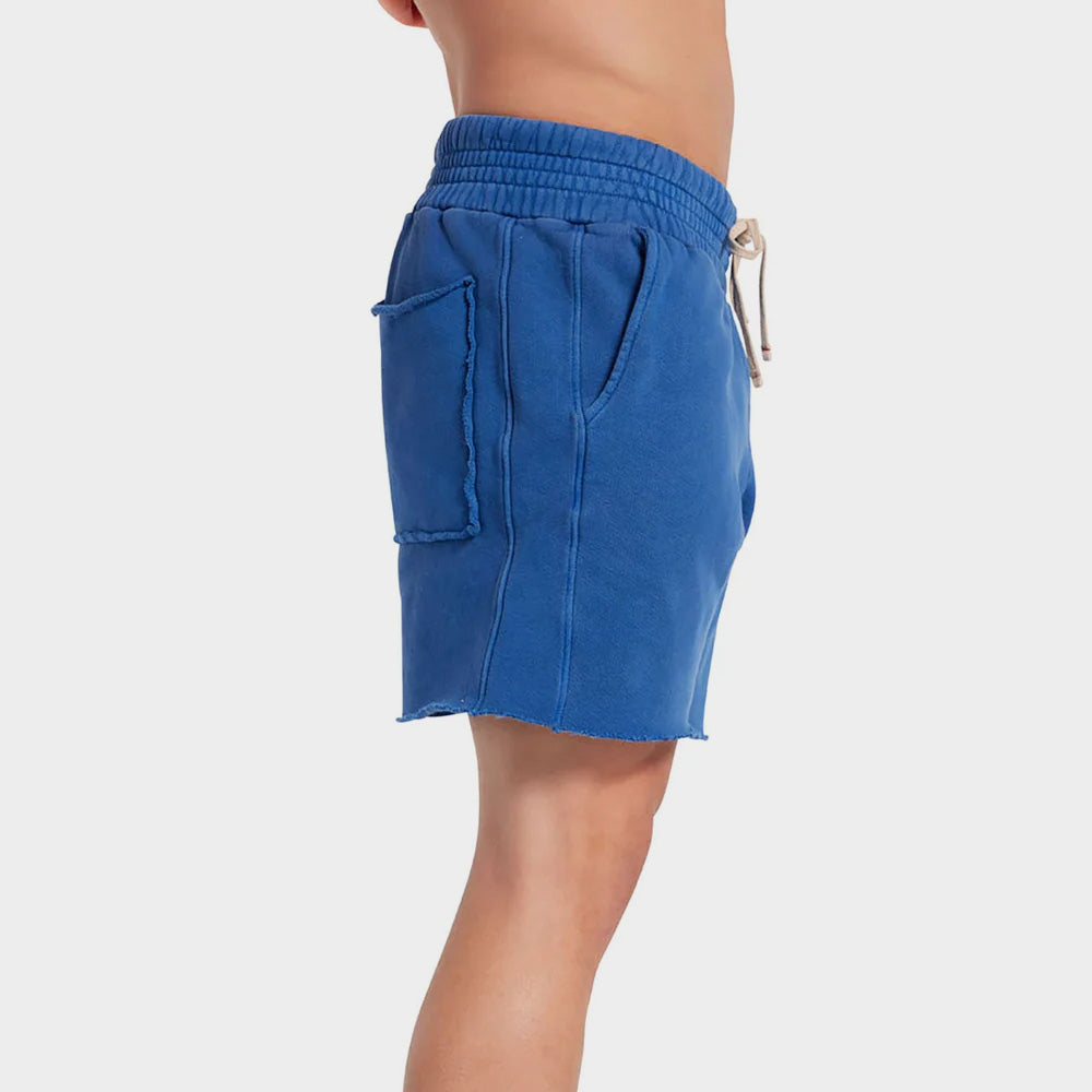 Side photo of a male model wears the electric blue cotton Yacht Short by Les Tien, featuring a wide elastic waistband and long white waist ties and side pockets.